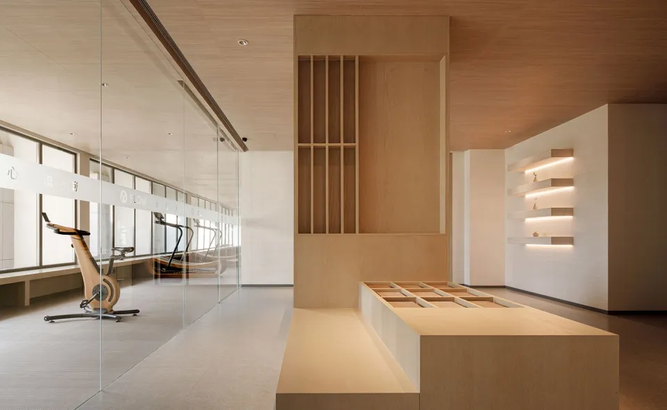 A modern fitness center featuring light-colored wood walls and glass partitions with exercise bikes and treadmills visible th