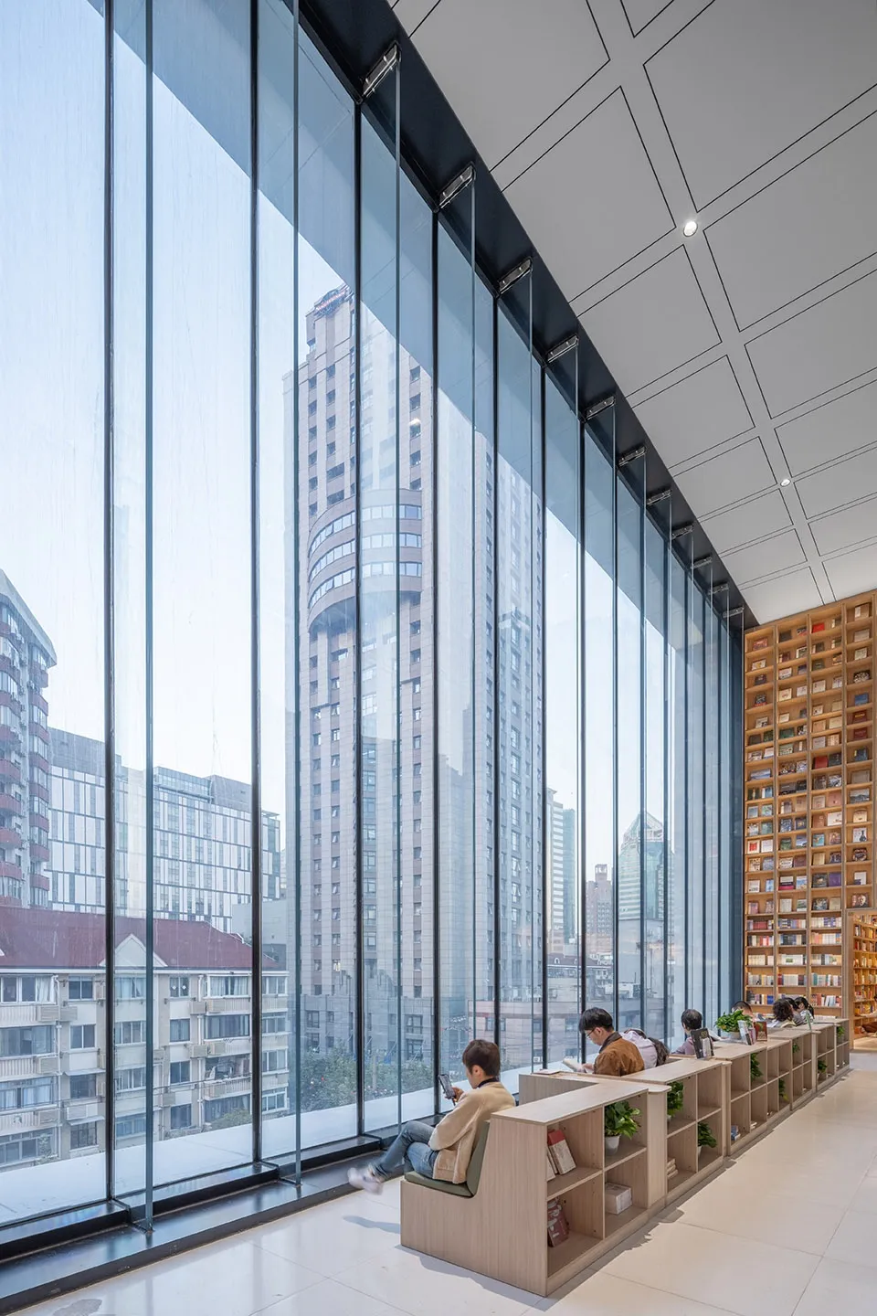 People sitting in a modern library with large glass walls overlooking the city.
