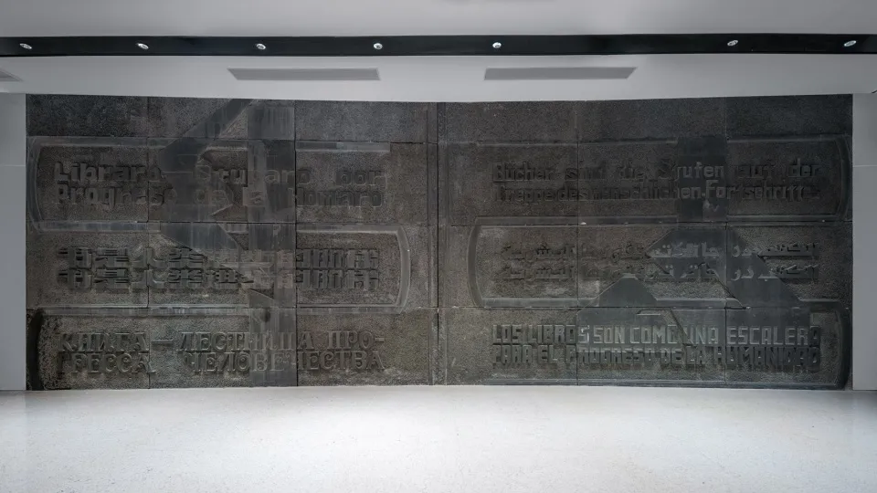 A dark metal mural featuring the words 'The Books Are the Steps of the Human Progress' in various languages