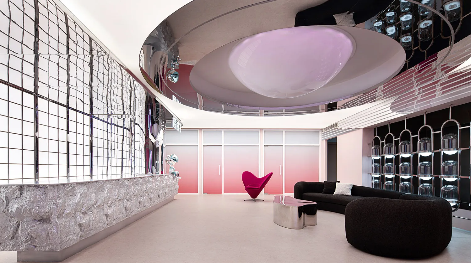 A contemporary lobby interior featuring a mirrored wall, pink ombre doors, and a pink chair.