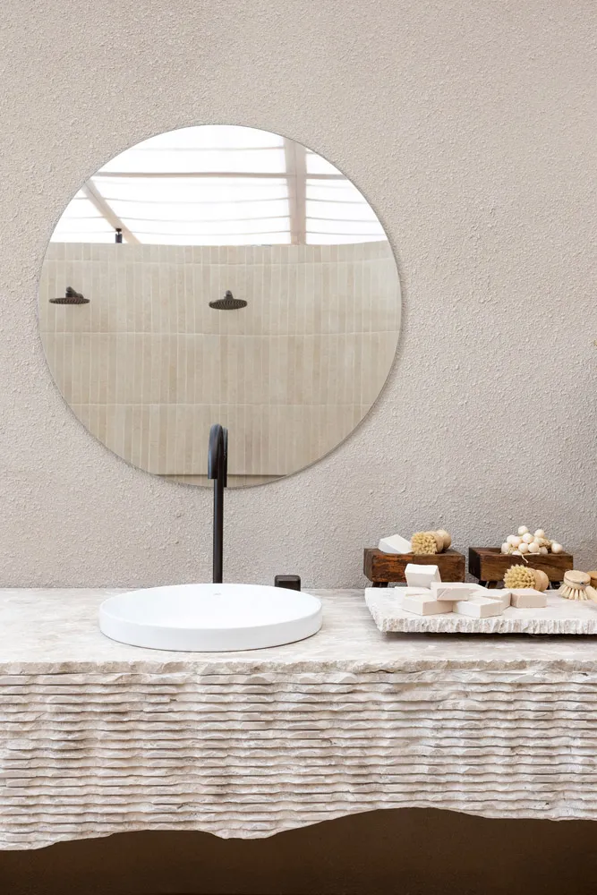 A minimalist bathroom with a concrete sink, round mirror, and natural lighting.
