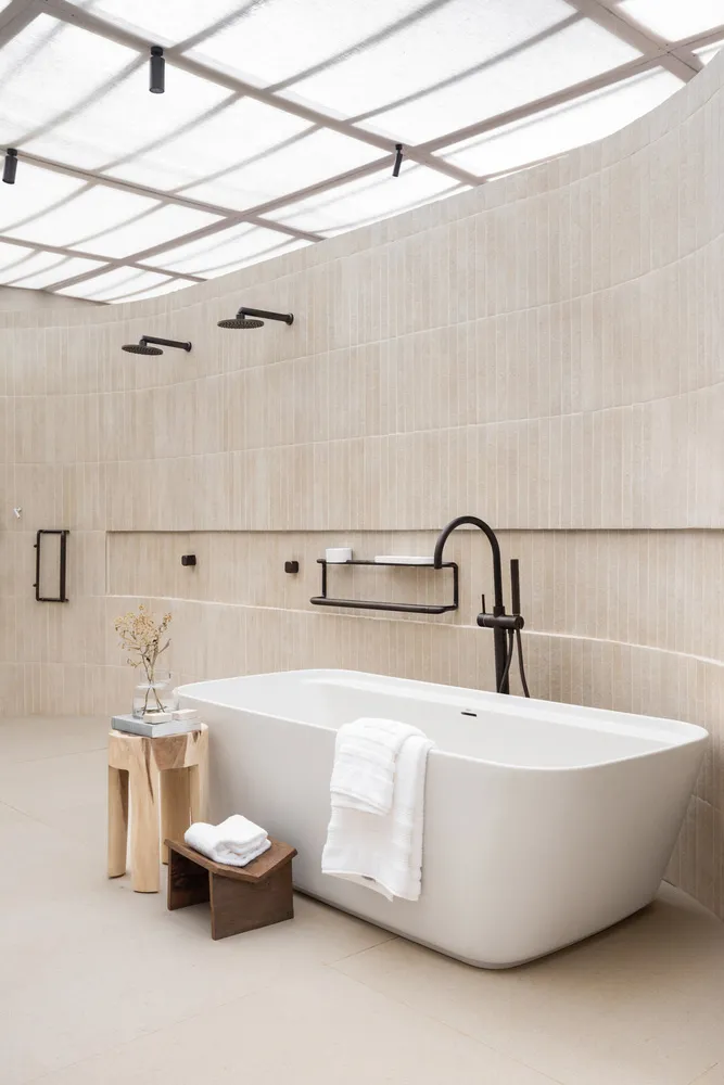 A modern bathroom featuring ceramic tiles, an oval-shaped bathtub, and multiple shower heads.