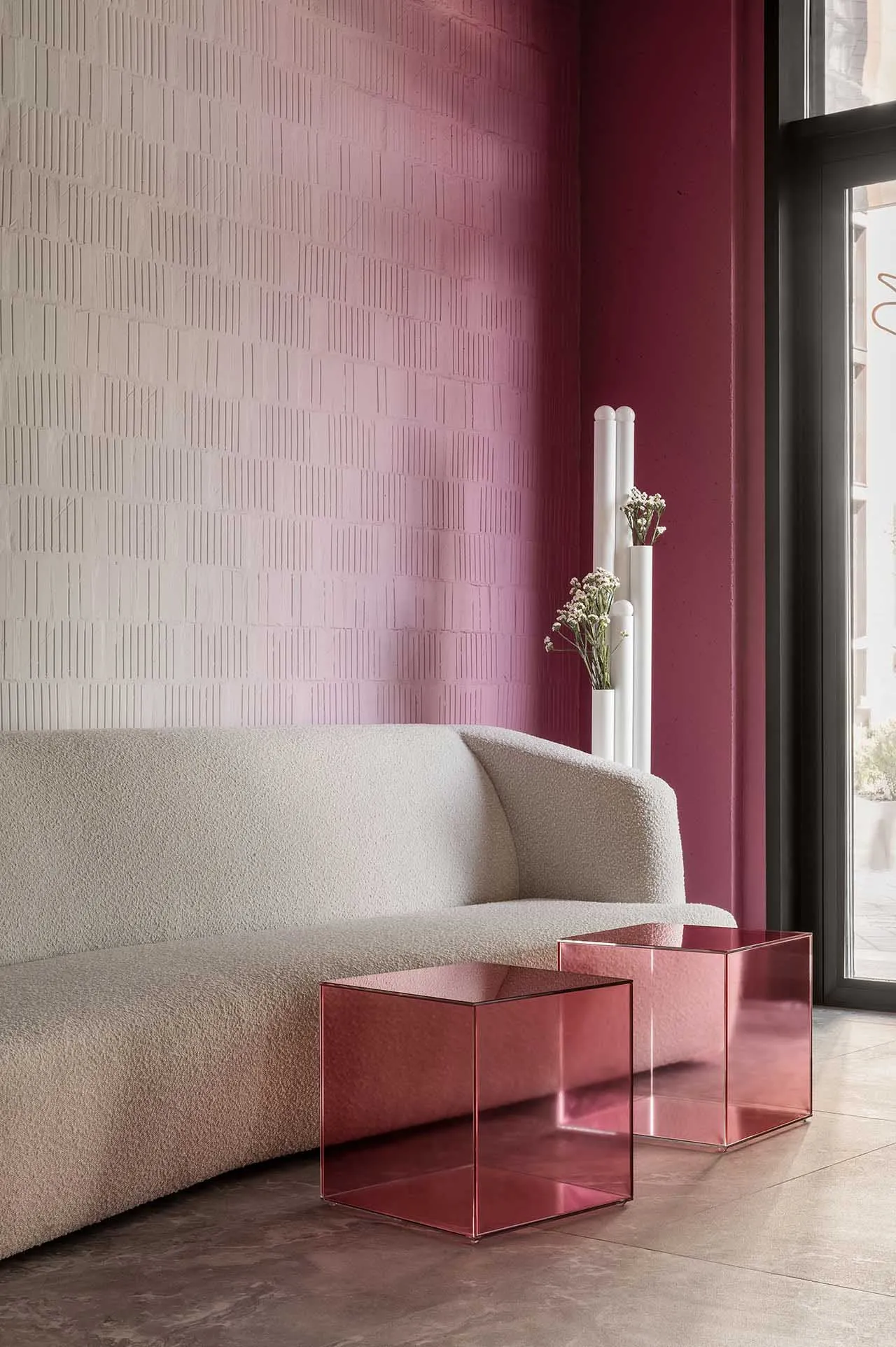 A minimalist living room featuring a textured wall, a beige sofa, and two pink acrylic cube tables.