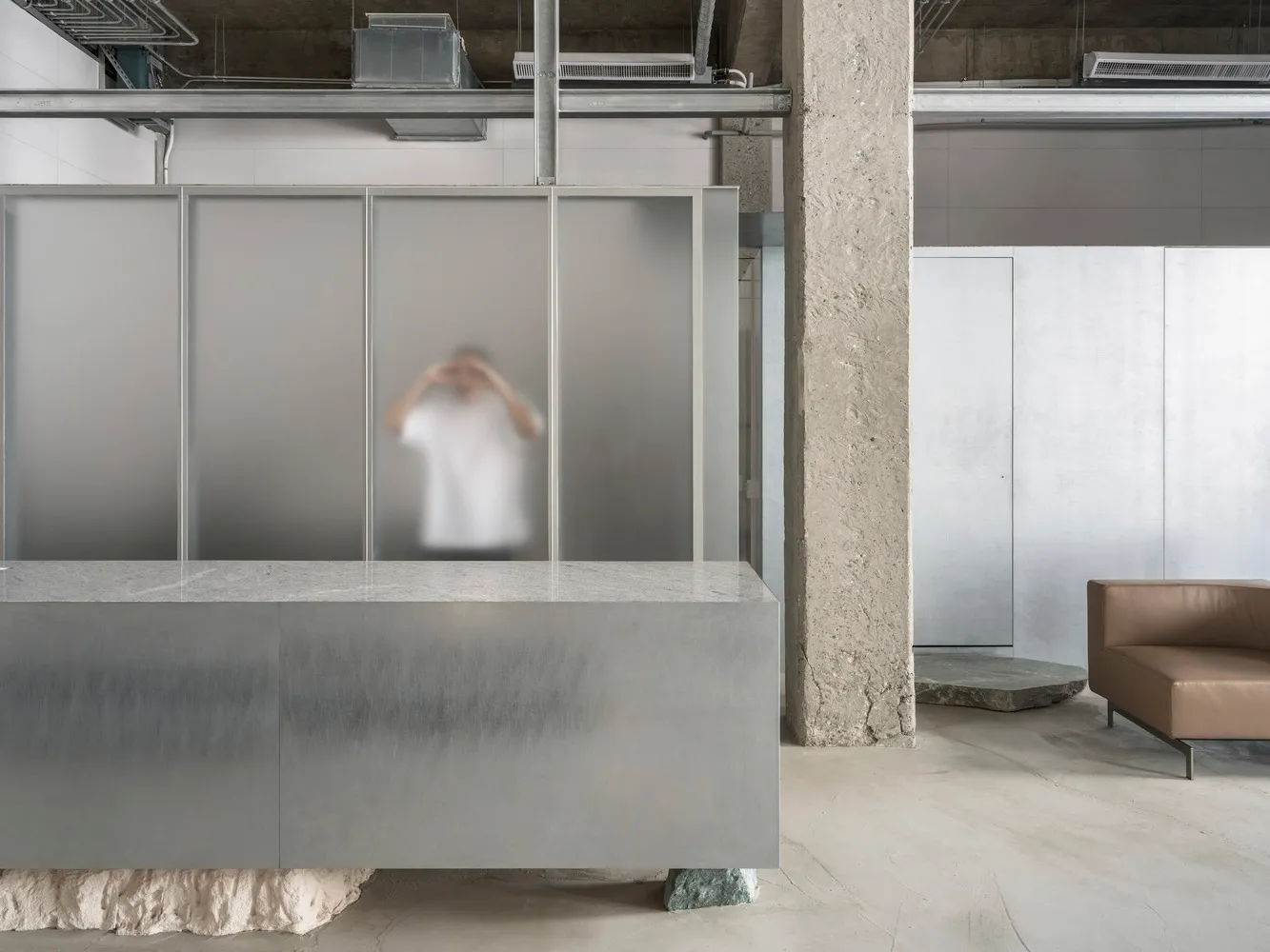 A modern office space featuring concrete walls, glass partitions, and metallic elements.
