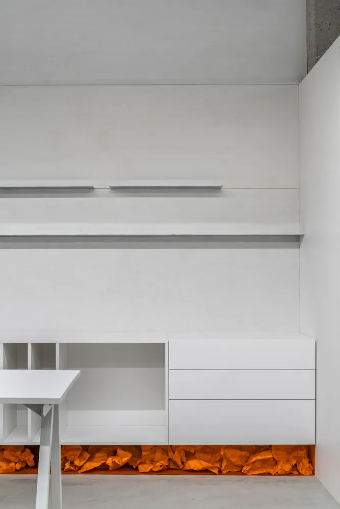 A minimalist office space featuring white concrete walls and shelves.