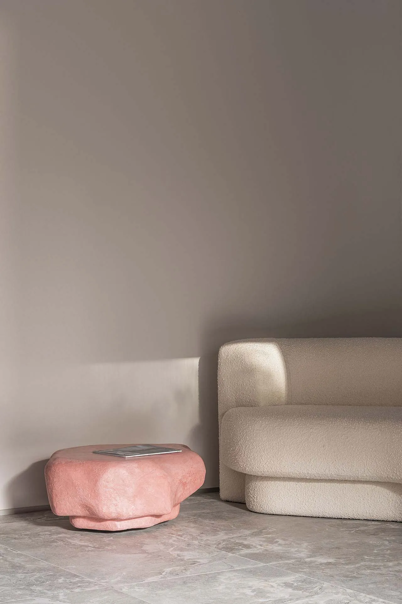 A modern sofa with a plush, white boucle upholstery paired with a pink, organic-shaped side table.