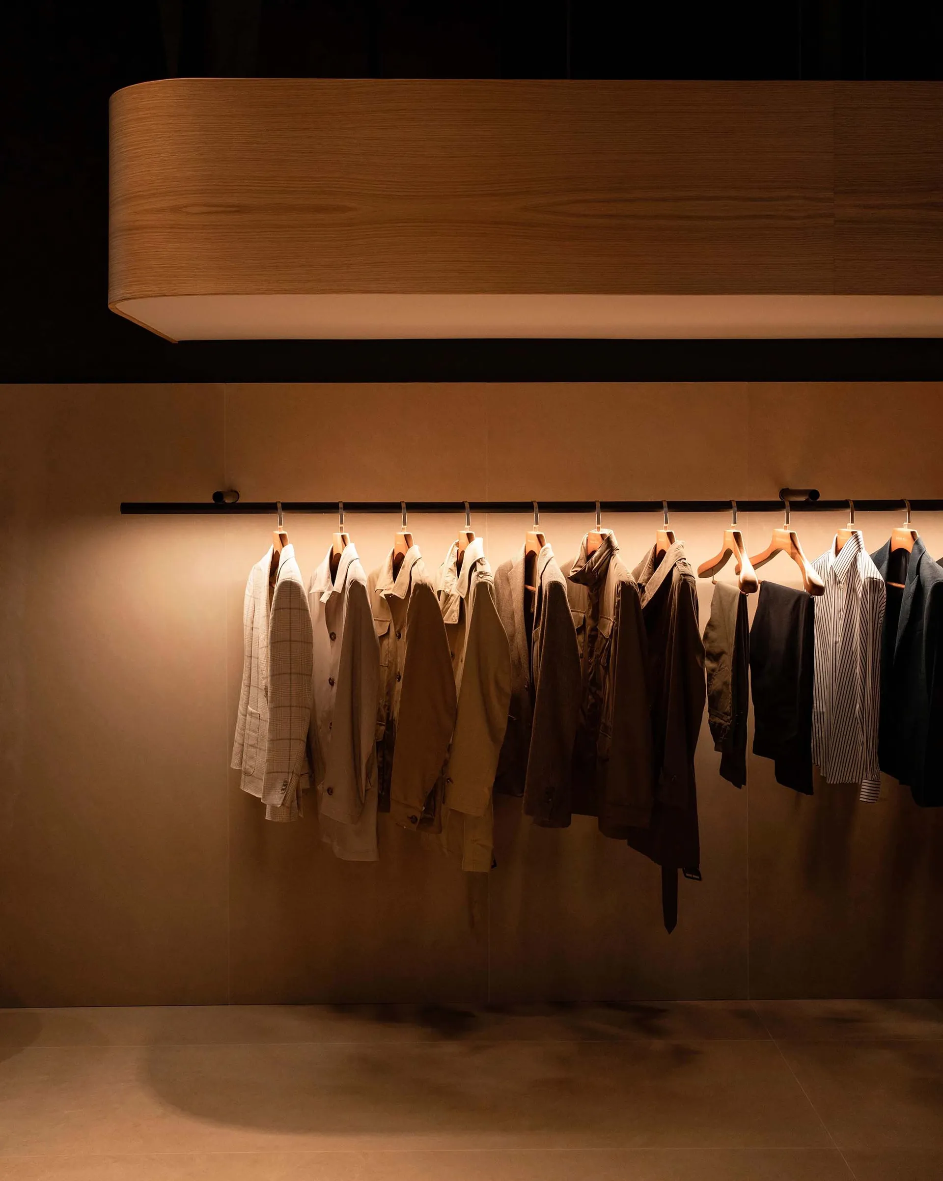 A row of clothing hangers displaying various garments, illuminated by warm lighting.