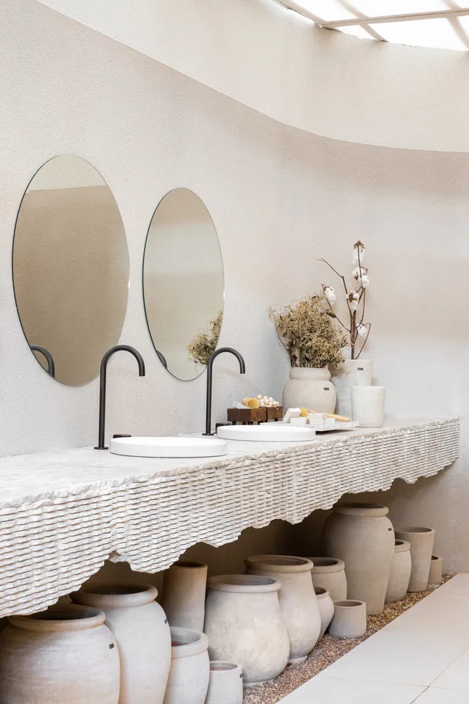 A minimalist bathroom with concrete sinks, pottery jars, and a wicker countertop.