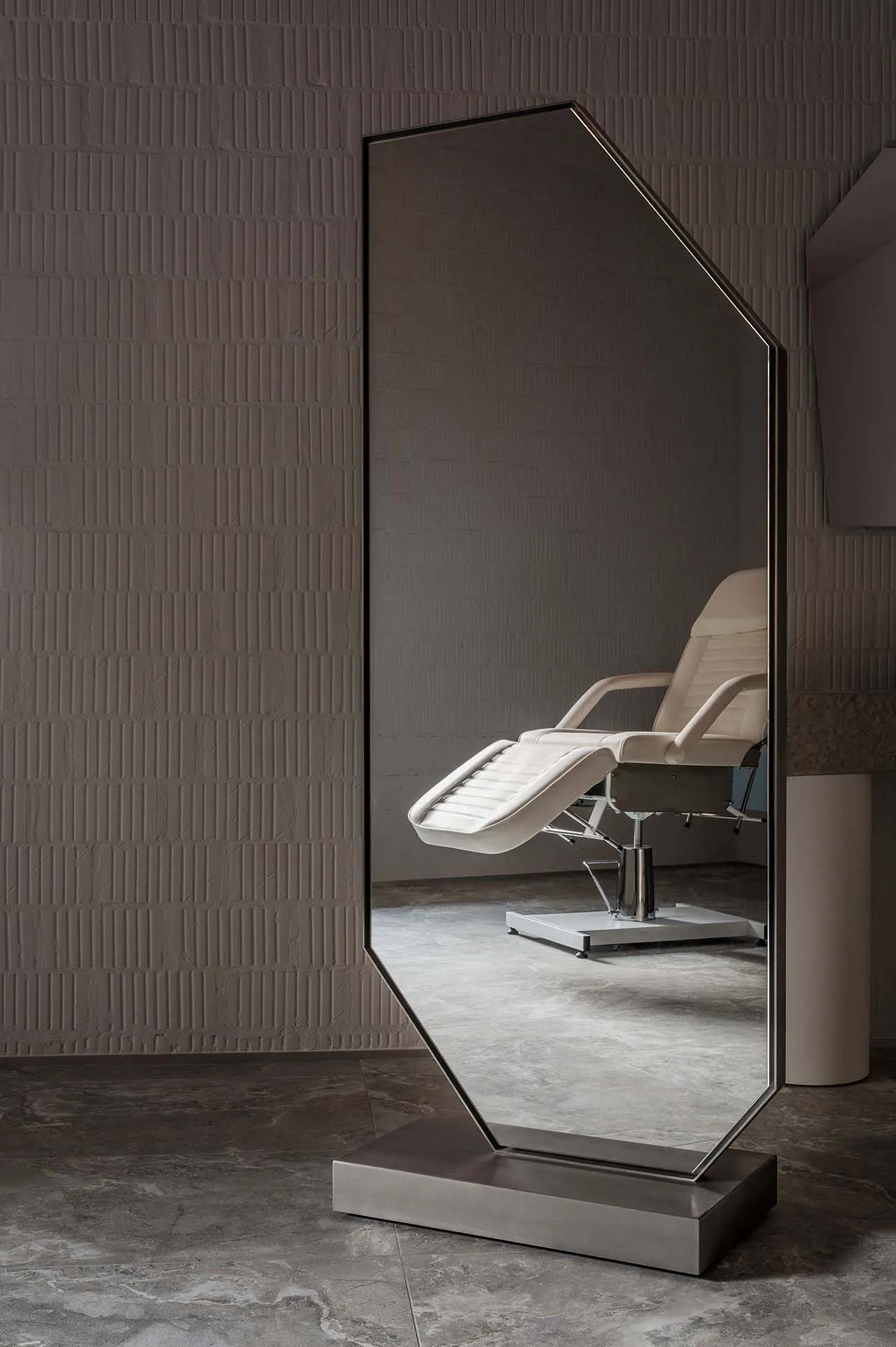 A minimalist floor mirror with a metal frame sits against a textured wall in a modern interior space.