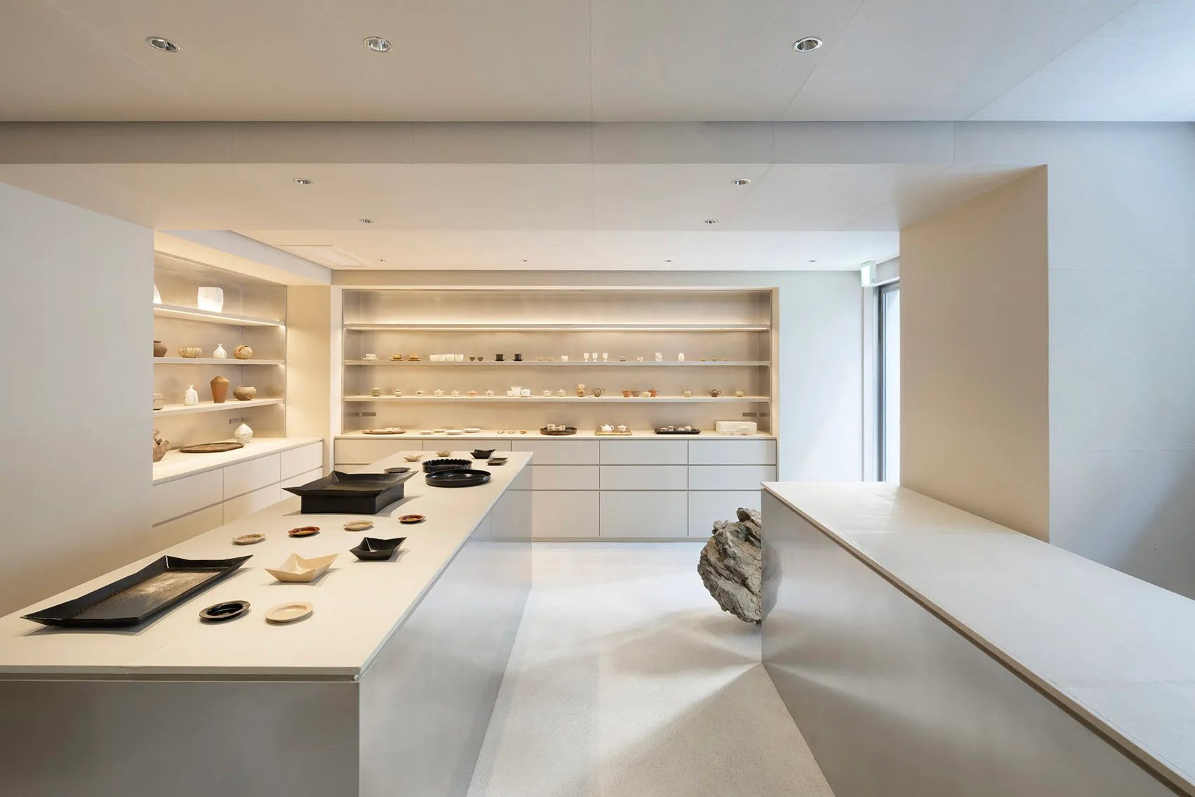 Minimalist room with various ceramic objects on display, showcasing sleek, white surfaces and clean lines.