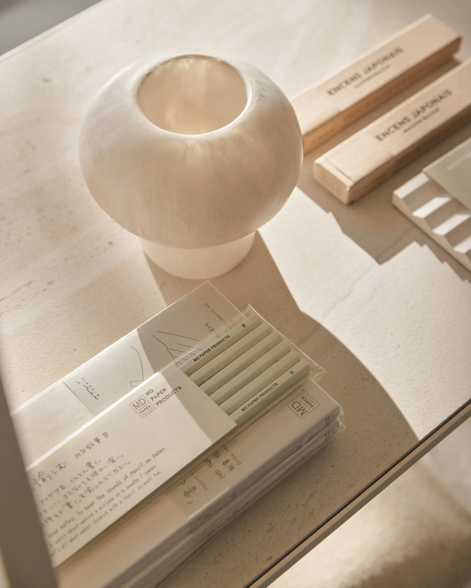 Minimalist desk accessories including pencils, stationary, and a vase on a light-colored tabletop.