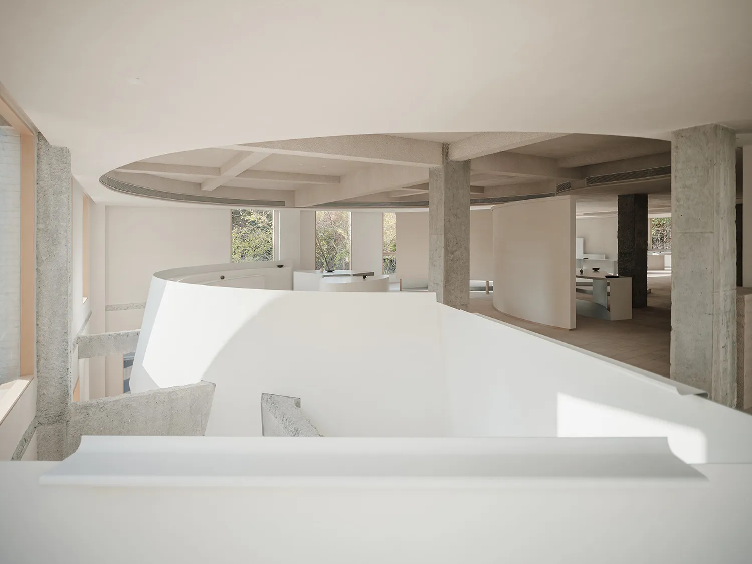 A modern interior space featuring concrete walls and floors, with a circular ceiling and natural light from large windows.