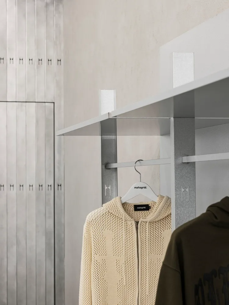 A minimalist clothing retail space with metallic shelves and a beige knit sweater hanging on a hanger.