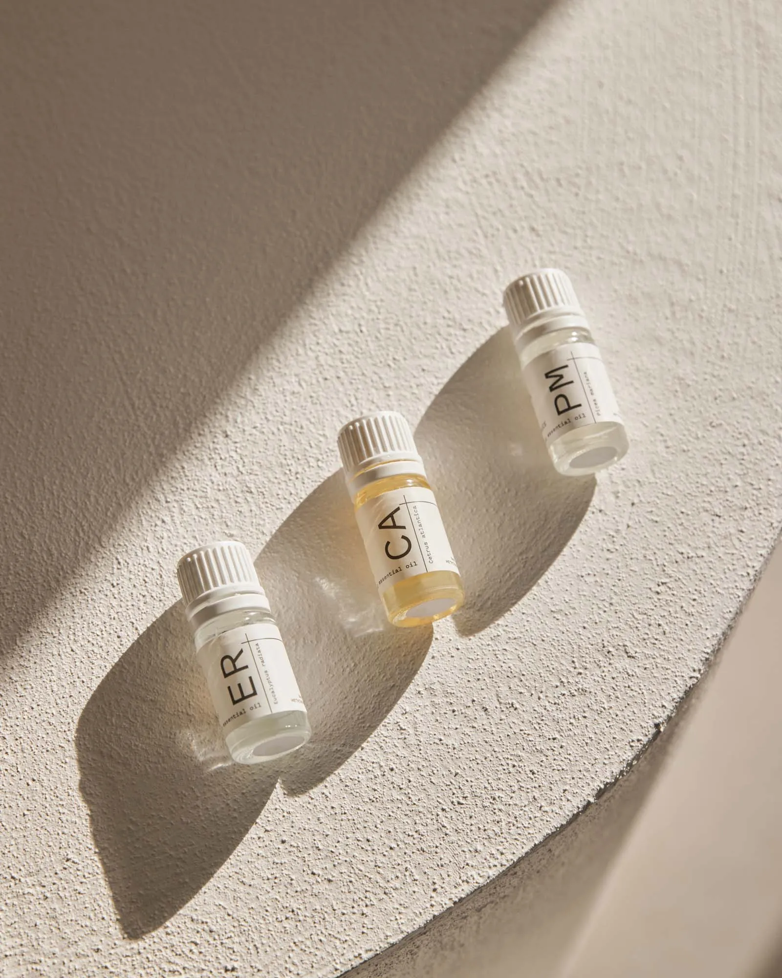 Three small glass bottles of essential oils with minimalist labels on a textured surface.