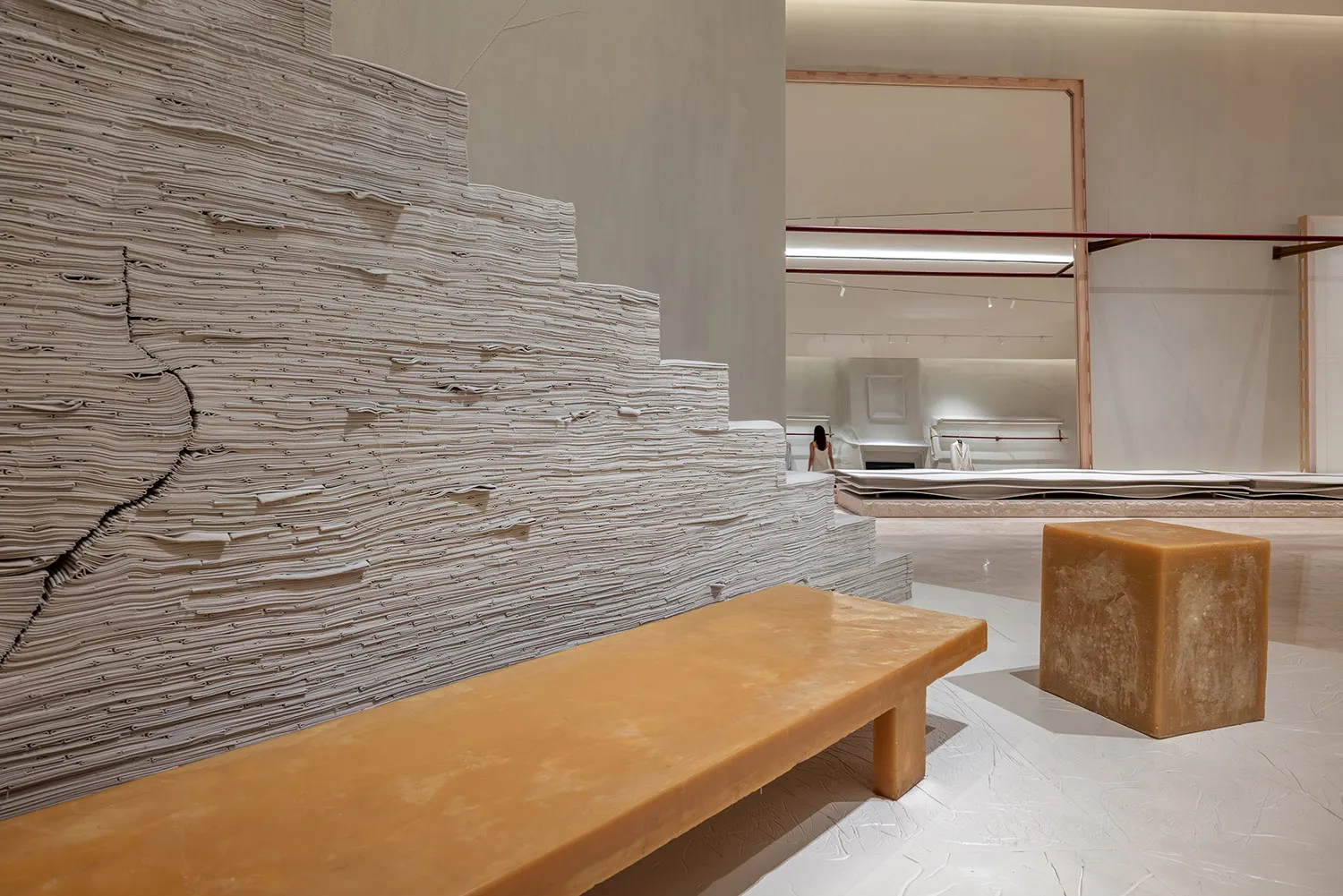 A minimalist installation featuring large stacks of paper and a natural wooden bench.