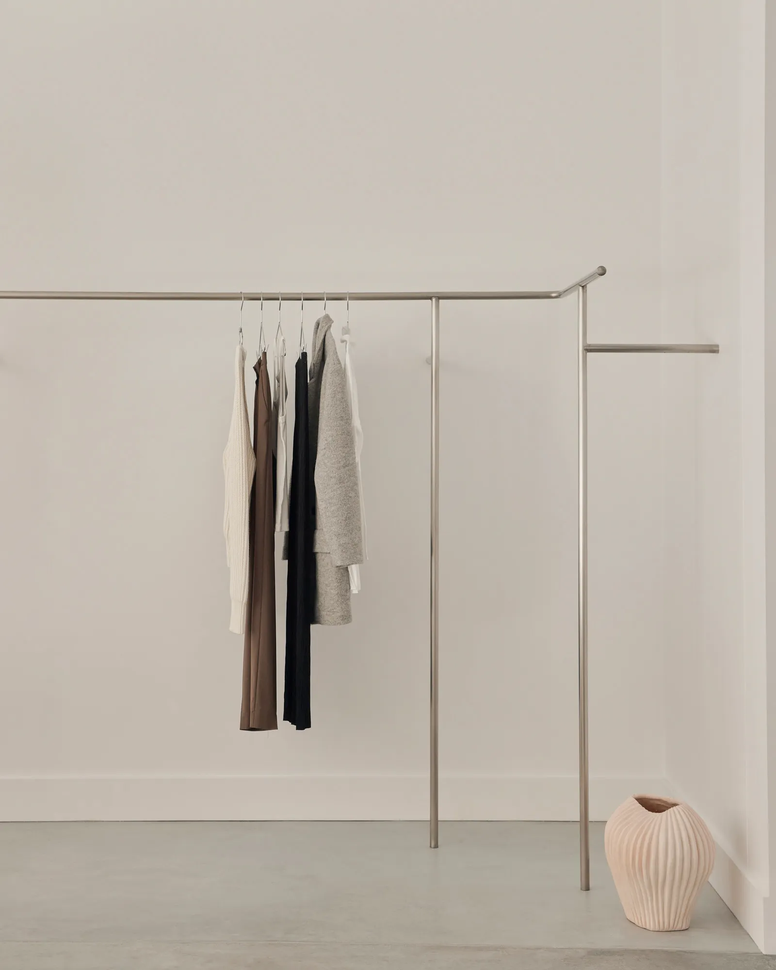 Minimalist clothing rack with metal rods and clothes hanging on it.