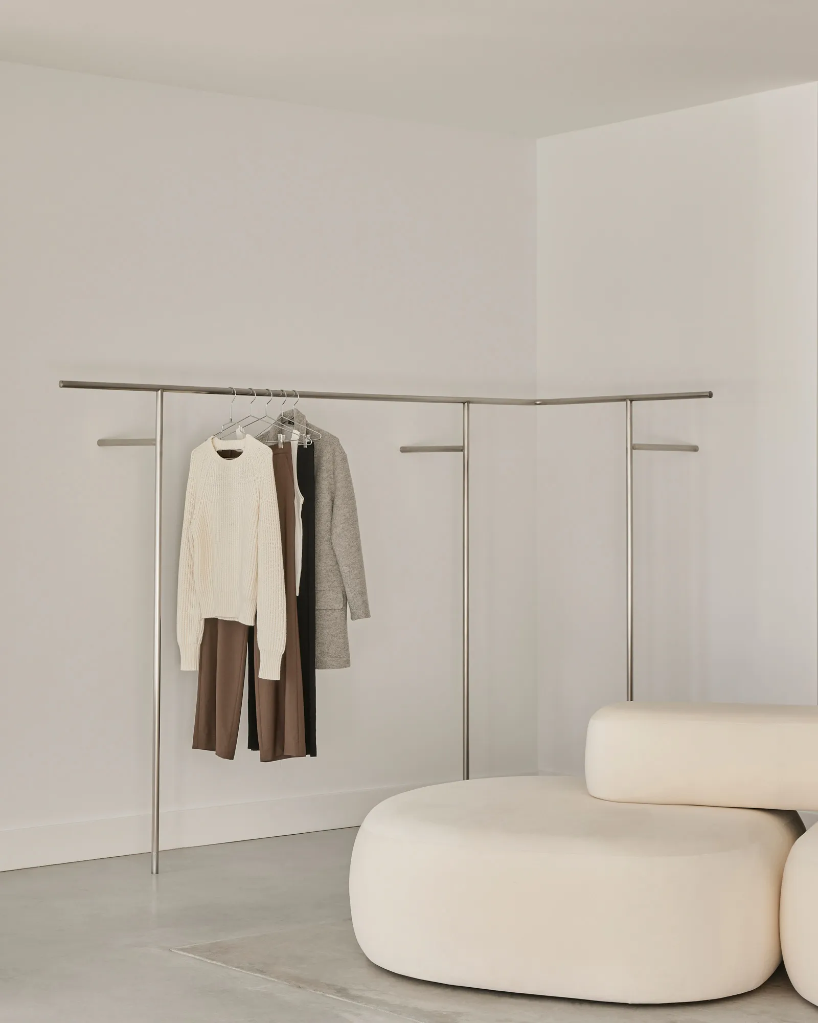 A minimalist clothing rack with white metal poles and black fabric hanging on it.