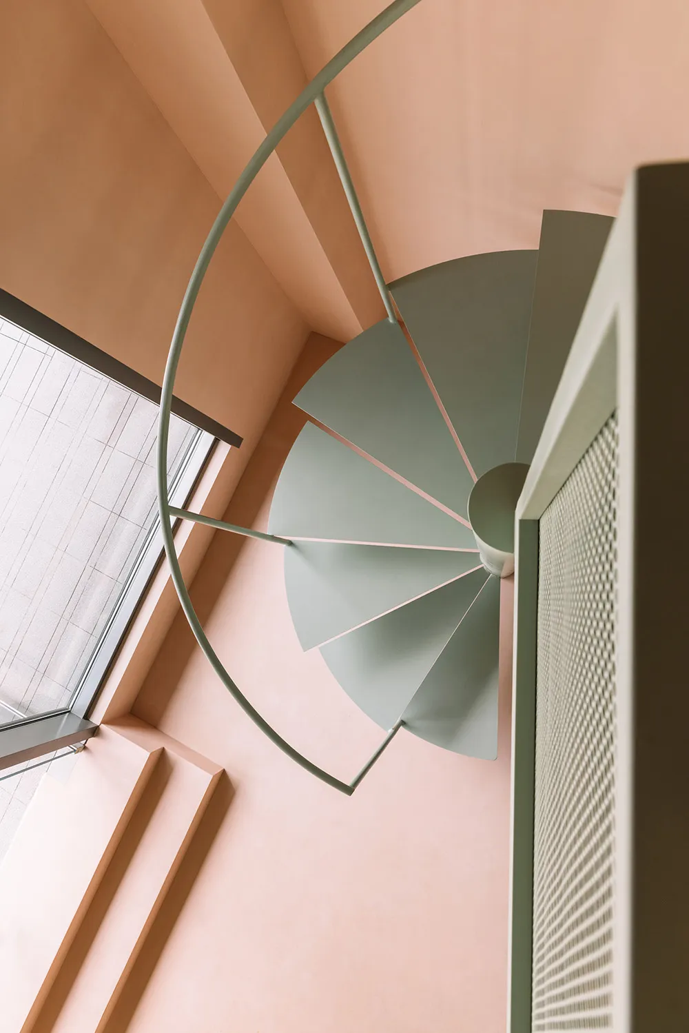 A modern metal staircase with pastel-colored steps and railings inside a room with peach-colored walls and a window with whit