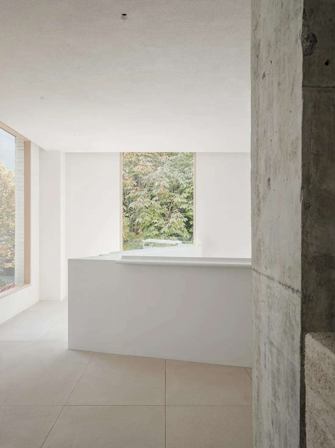 A modern reception area with a minimalist design, featuring concrete materials and a sleek, white desk.