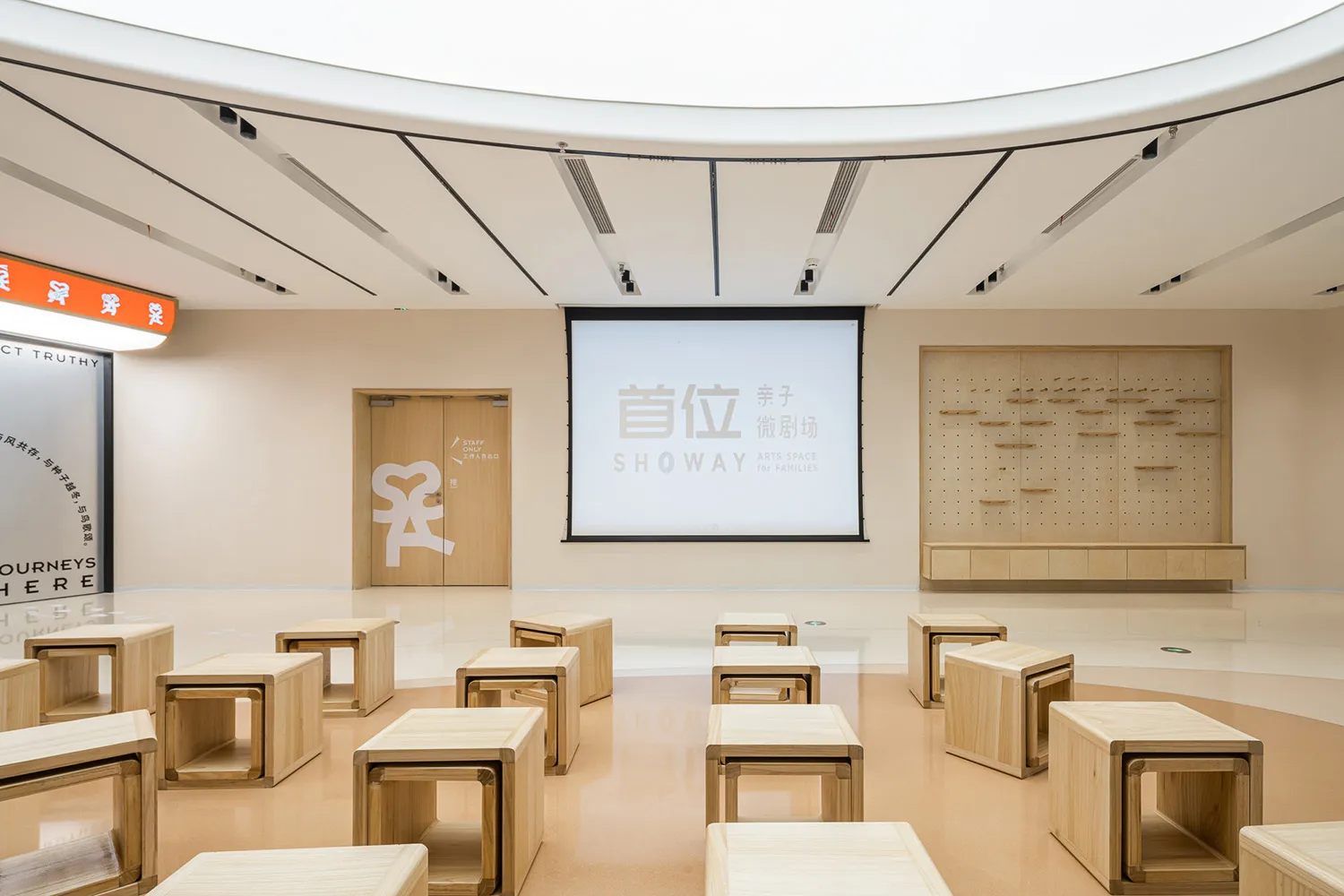 A minimalist education space with wooden tables arranged in a semi-circle around a projector screen.