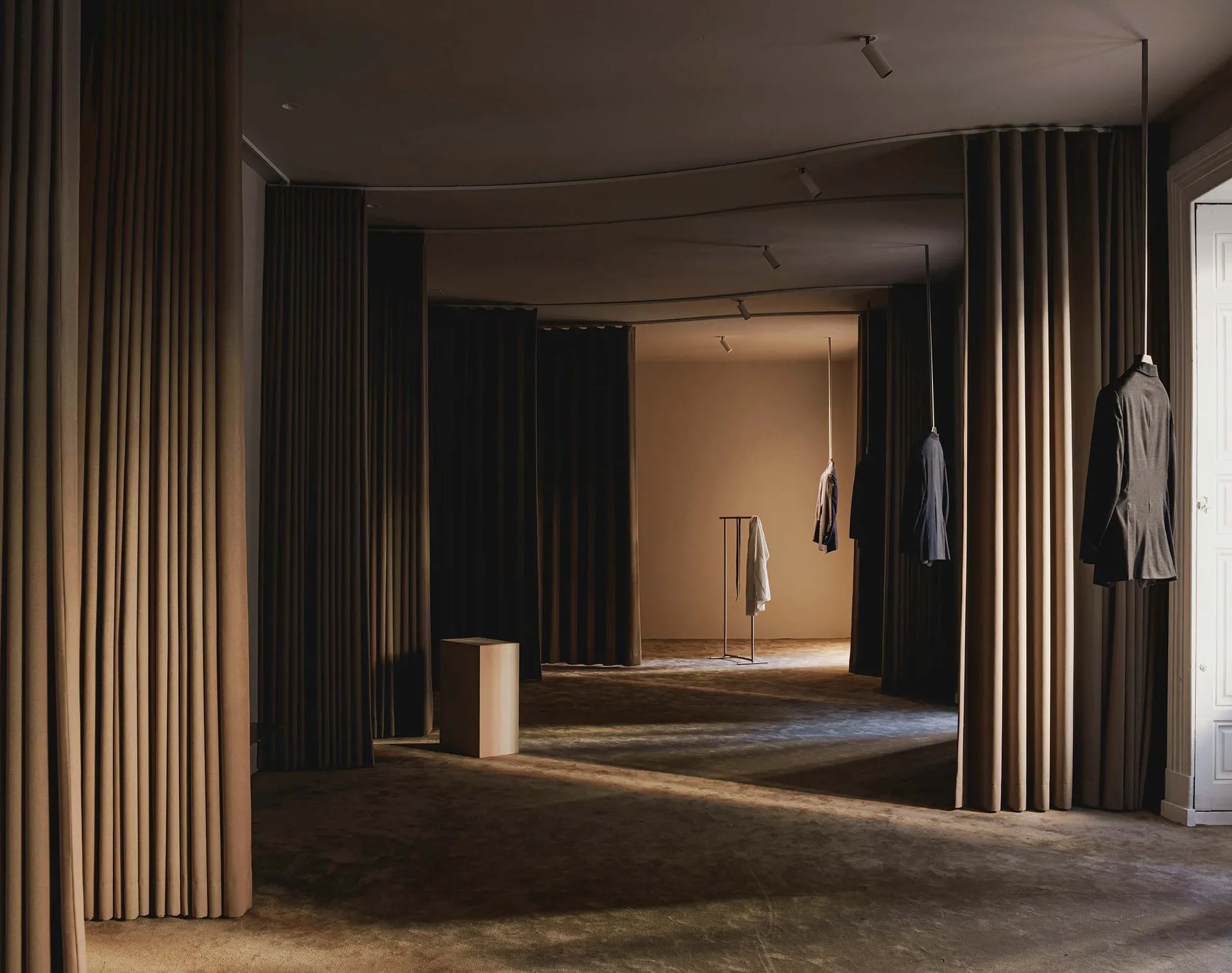 A minimalist clothing boutique featuring draped curtains and exposed ceiling lights.