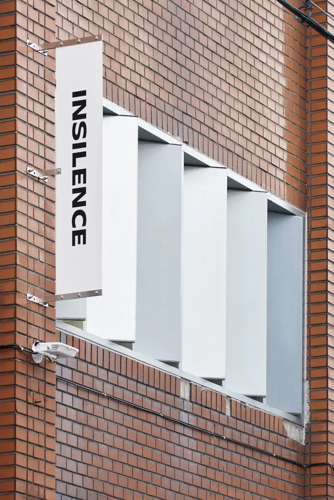 A white sign with the word 'INSILENCE' is mounted on a brick wall.