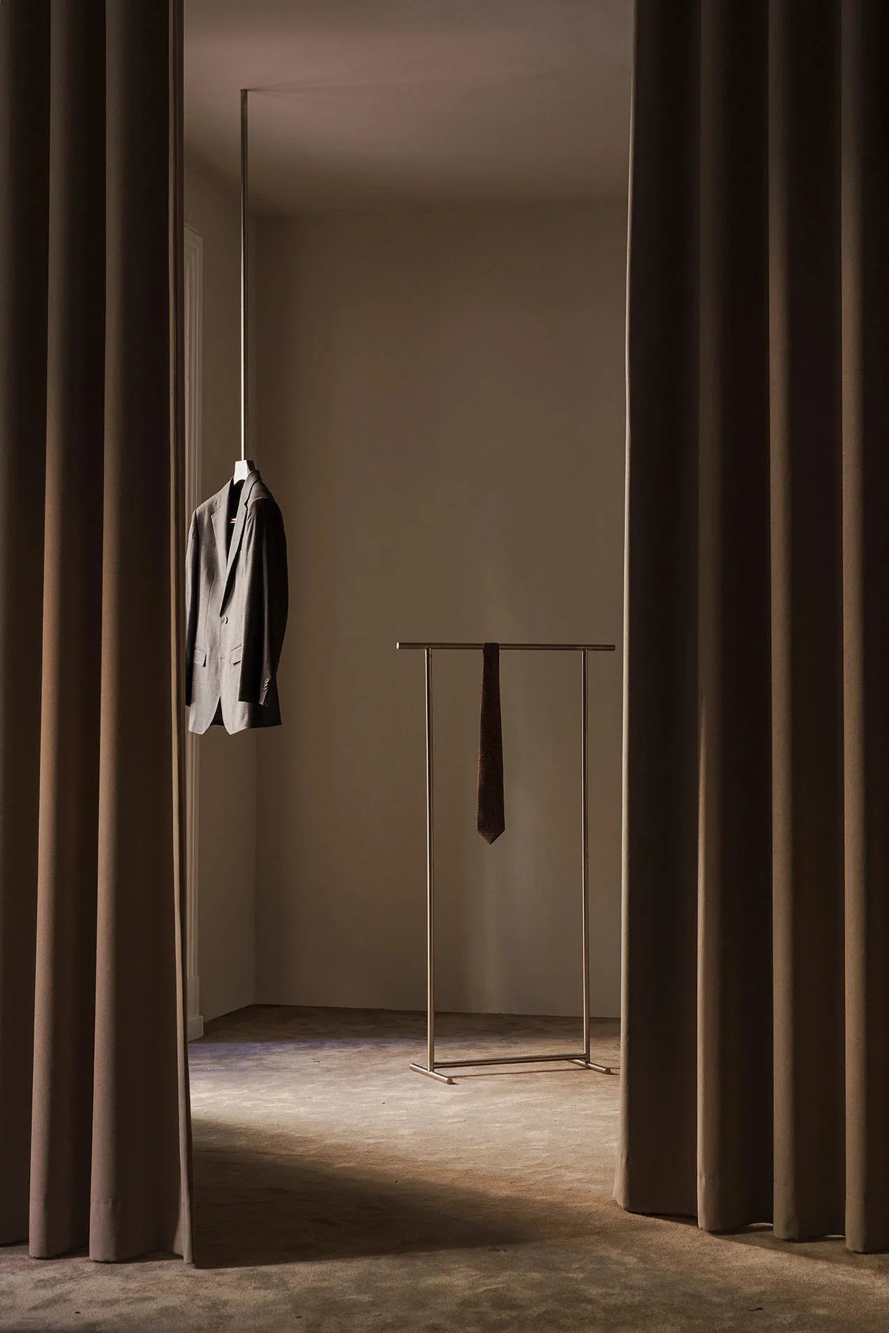 A minimalist clothing display featuring a metallic stand and a suit jacket hanging from a rod.