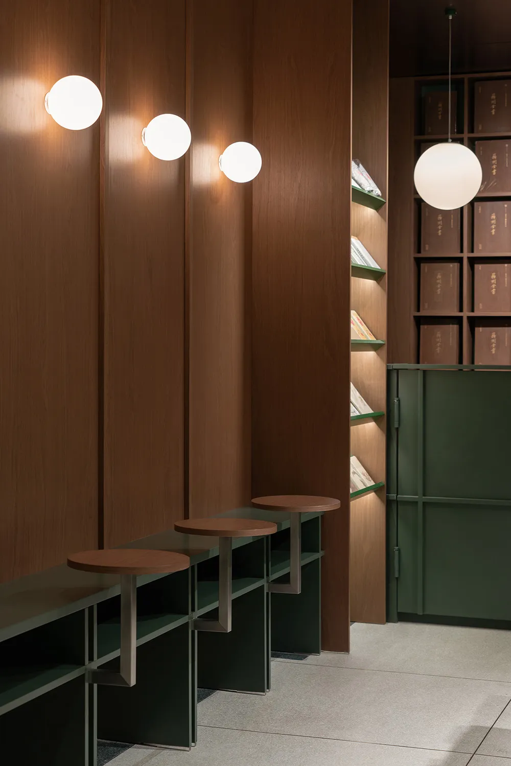 Modern minimalist library with wooden walls and metal tables, featuring spherical lighting fixtures.