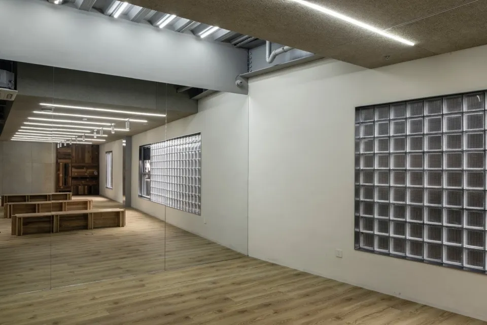 A minimalist workout room with glass blocks and wooden benches under bright lighting.