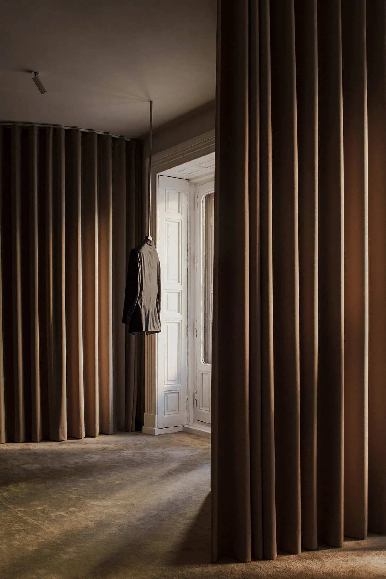 Modern interior space featuring a hanging suede jacket on a white door with high curtains.