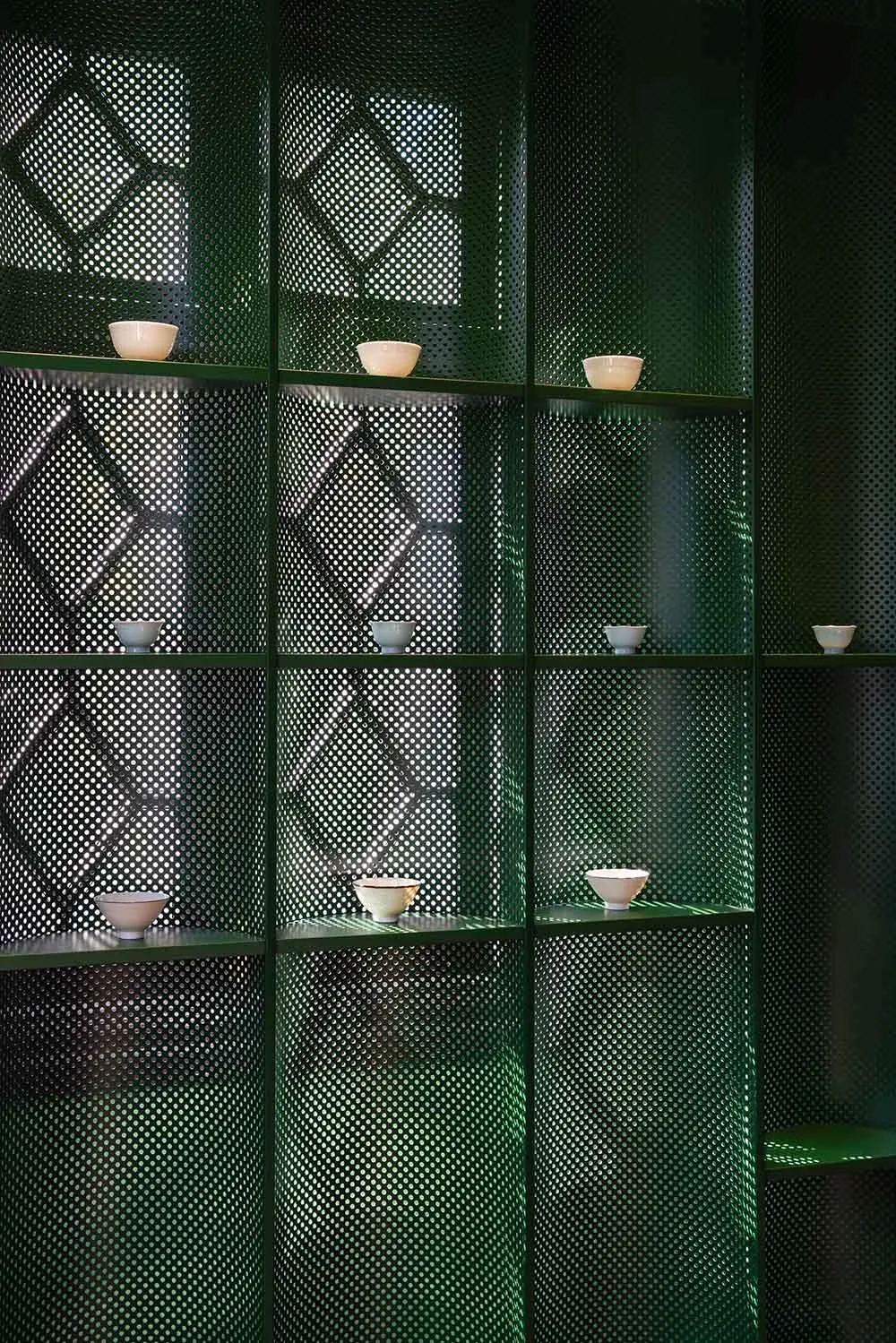 A modern interior design featuring perforated metal shelving with small white bowls.