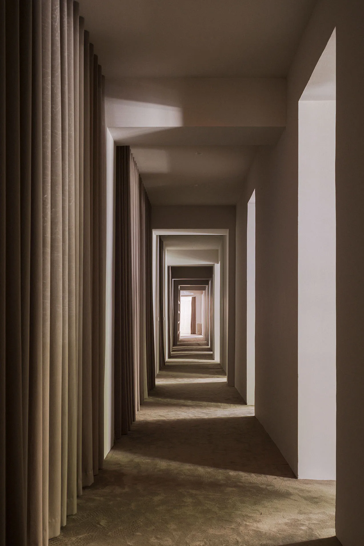 A minimalist corridor with neutral-toned walls and curtains, featuring repetitive architectural elements.