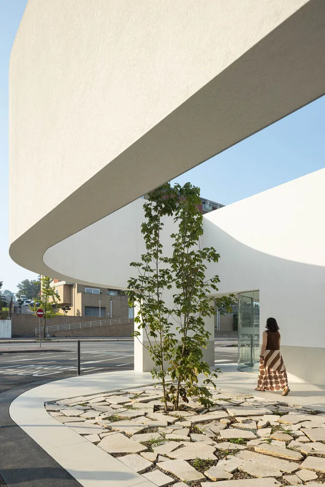 A woman walks past a modern entryway featuring a tree planted in a bed of concrete and glass tiles.