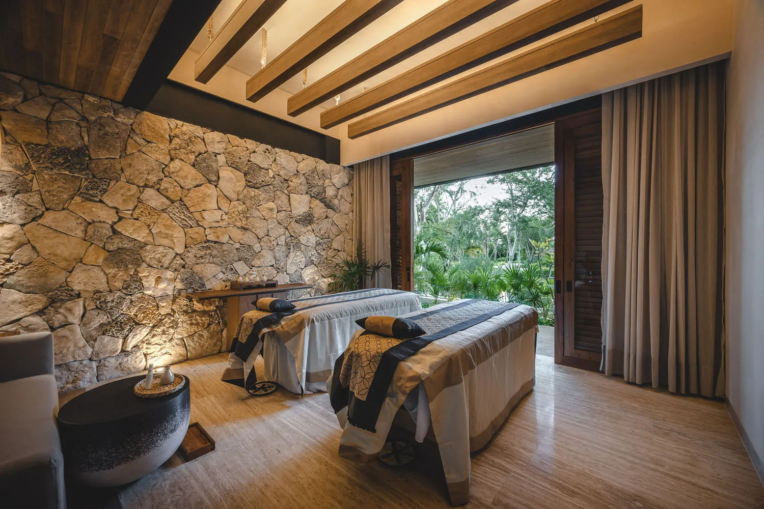 A modern spa suite featuring stone and wood materials, with a view of lush greenery outside.