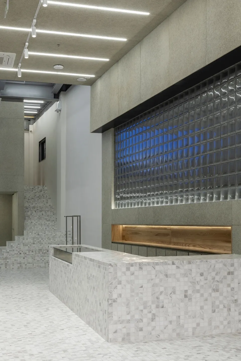 A modern reception desk made of concrete with glass inserts and a wooden counter.