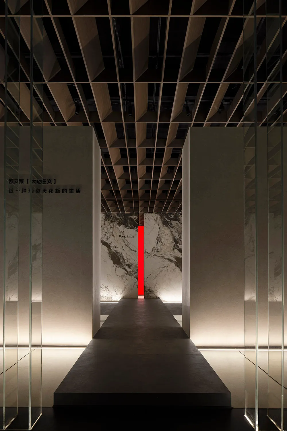 View down a minimalist hallway in an exhibition space, featuring stone walls.
