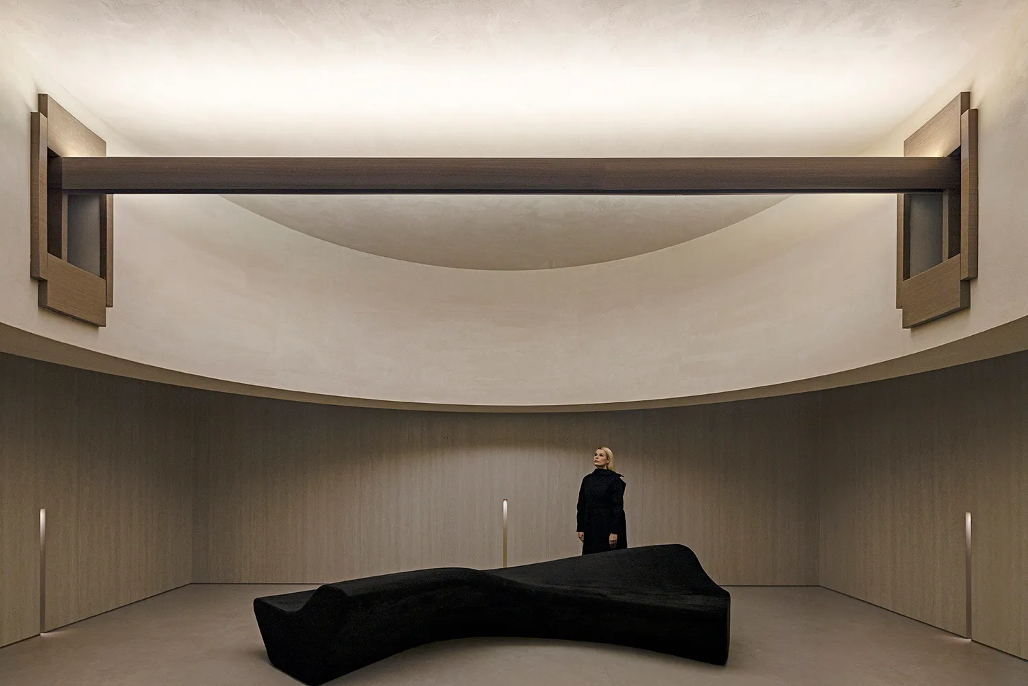 Modern art installation featuring a dramatic, abstract concrete sculpture suspended from the ceiling in a minimalist space.