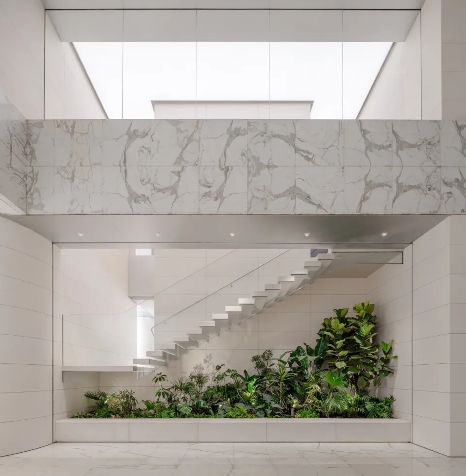 A modern and minimalist interior space with marble walls and floors, featuring a glass ceiling and green plants.