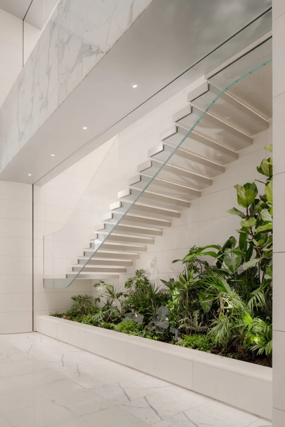 Modern staircase with glass railings surrounded by greenery and tile flooring.