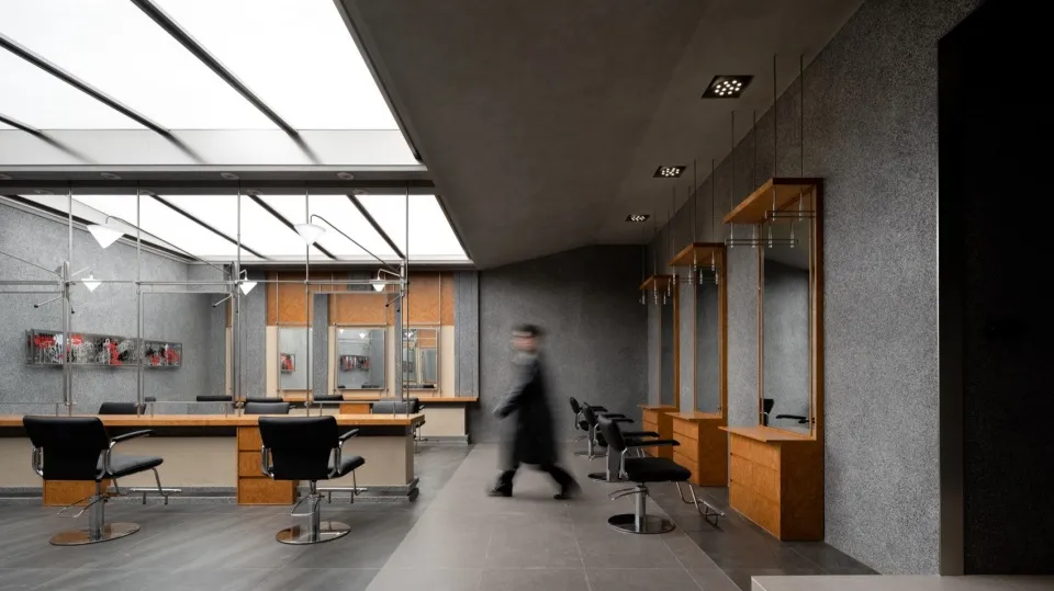 A modern salon interior featuring sleek concrete flooring and walls, with black chairs and illuminated ceilings.