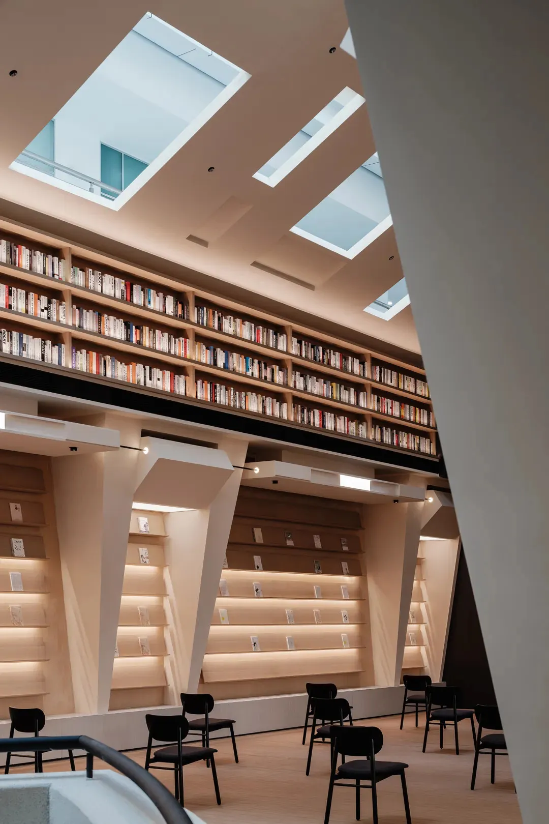 現代圖書館室內,木質與玻璃書架陳列滿滿書籍,由天窗自然光線照亮。