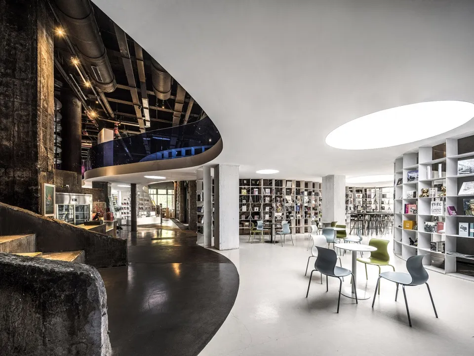 Industrial-style library with concrete and metal materials, featuring seating and bookshelves.