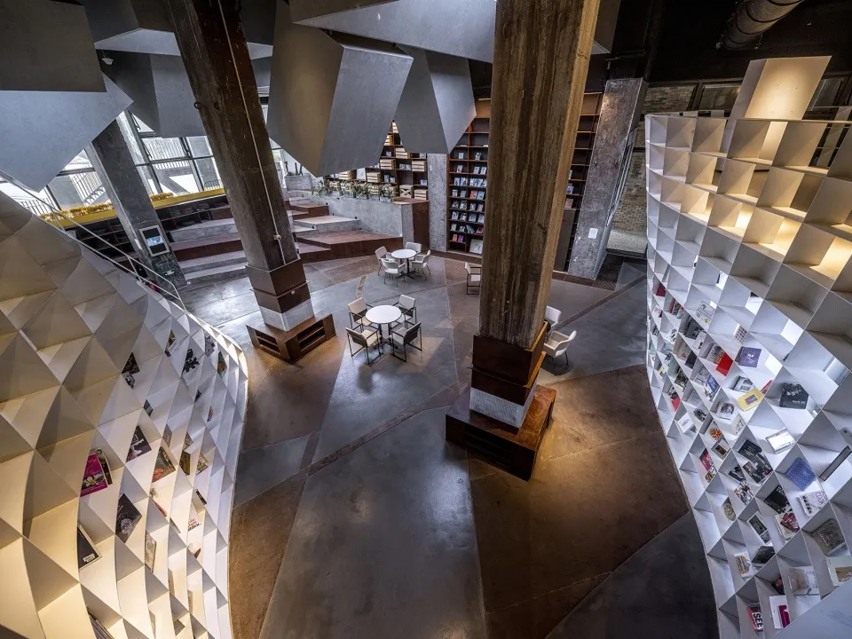 A modern library interior with concrete finishes and geometric bookshelves.