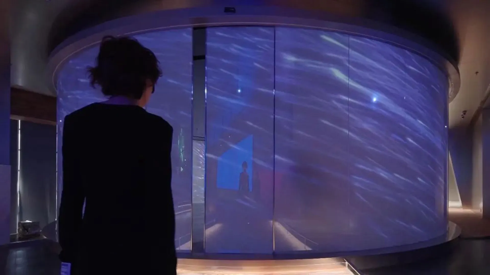 A person stands in front of a large, digital projection screen displaying an abstract design with a starry, space-themed back