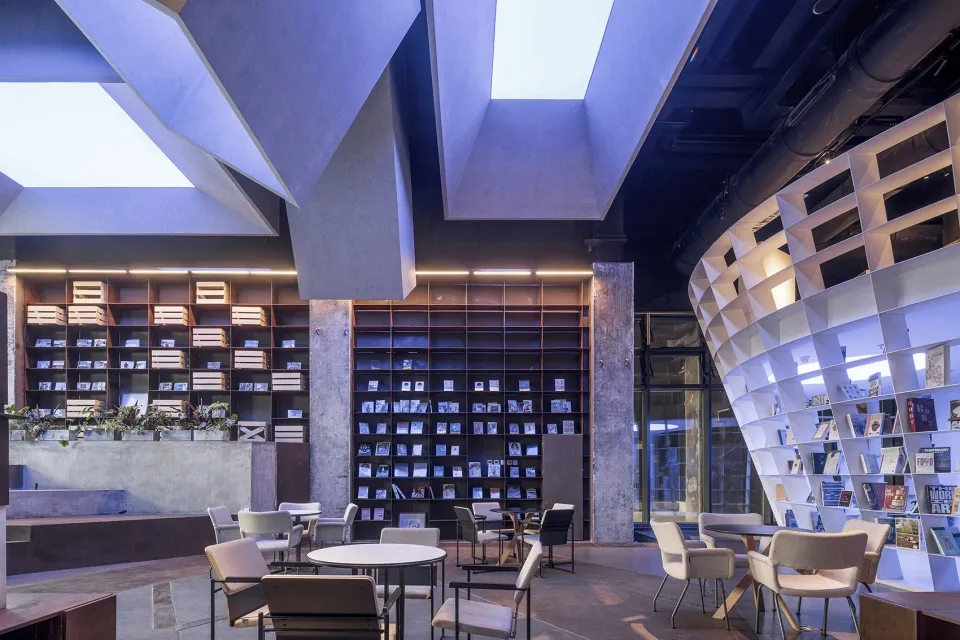 A modern library space with concrete walls, wooden furniture, and large bookshelves.