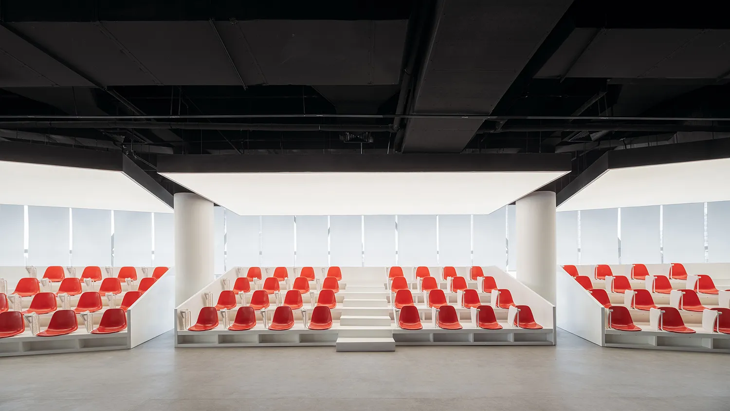 A modern conference room with red plastic seats arranged in rows with white railings.