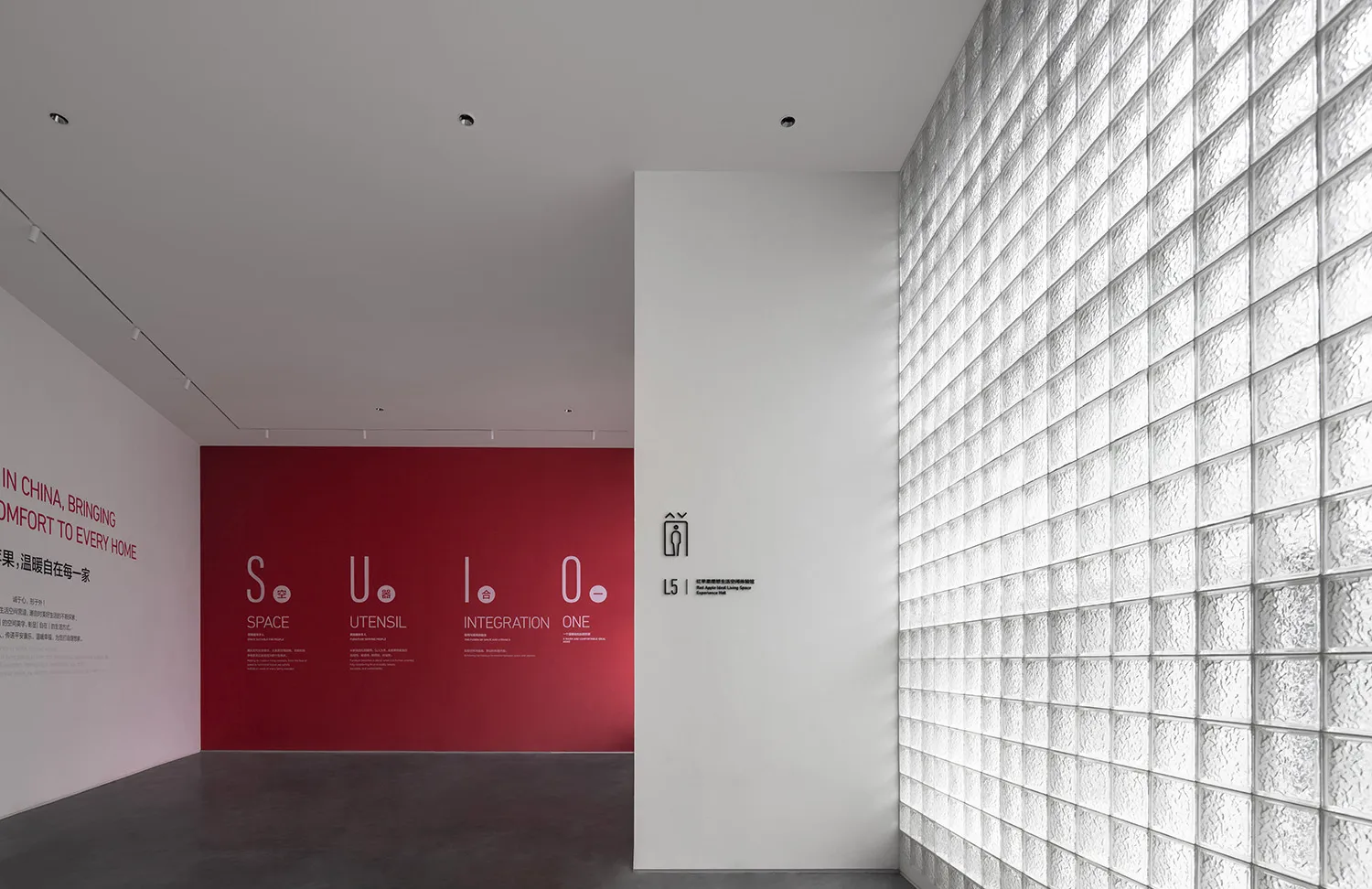 A modern event space with transparent glass block walls and red informational posters on a deep grey floor.