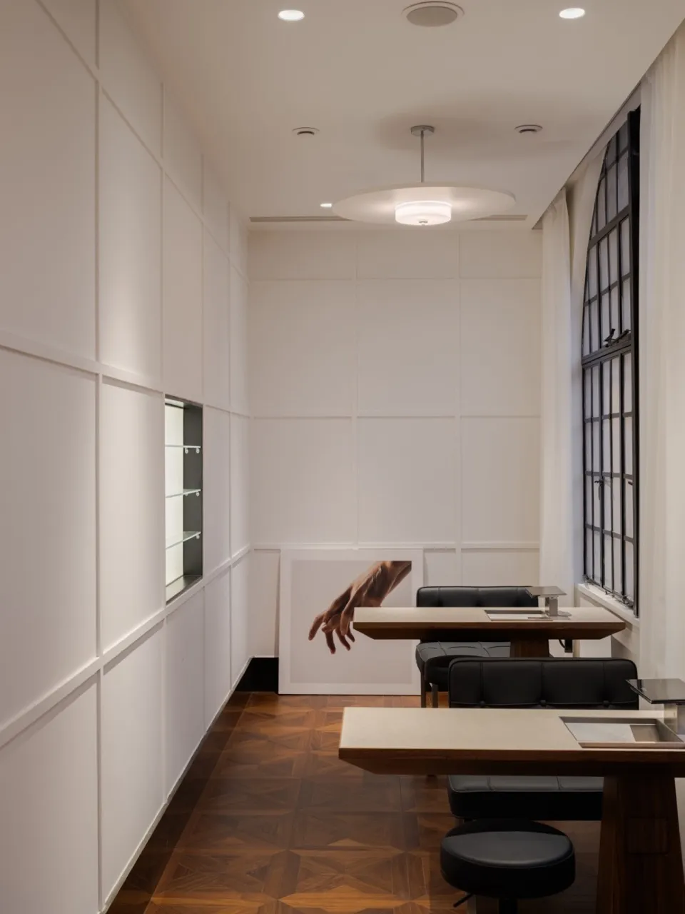 A modern office space with white paneled walls, wooden flooring, and black seating.