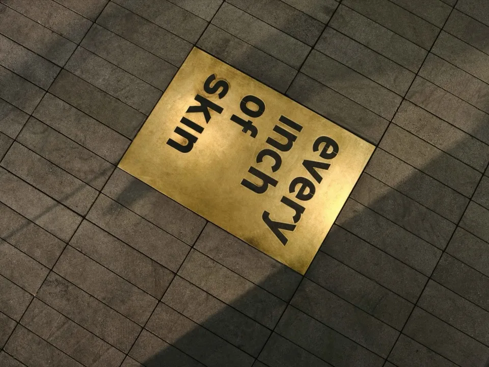 A metallic square with the words "Every Inch of Every Skin" on a tiled surface.