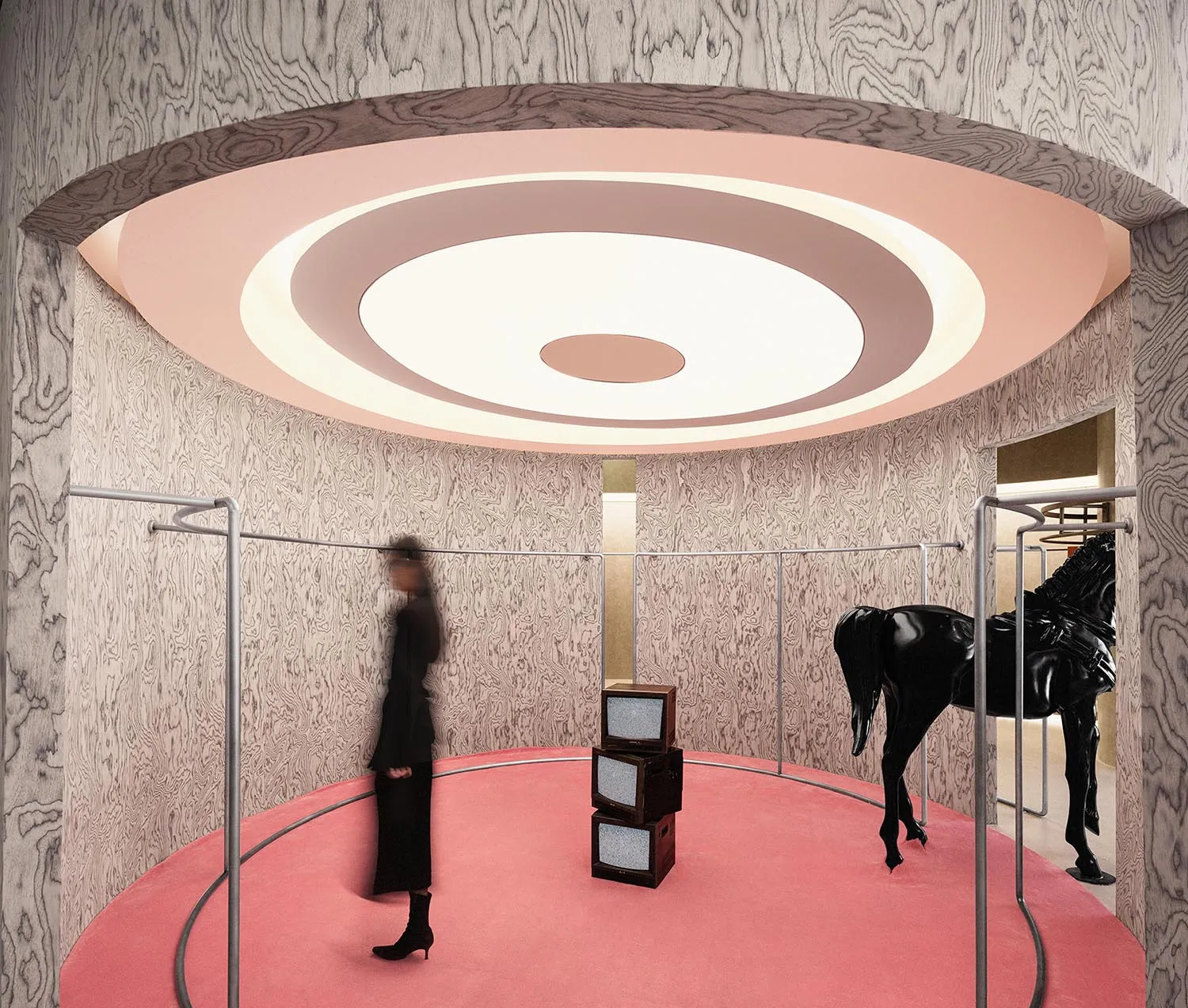 A modern art installation featuring a black horse made of plastic standing on a red carpet in a room with a large eye-shaped